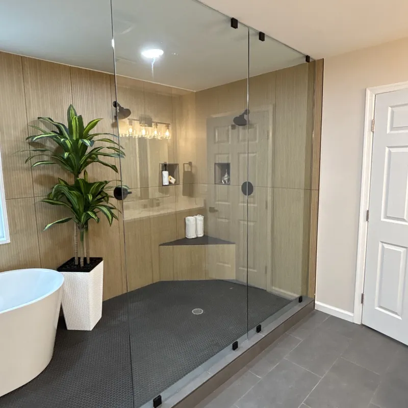 A large walk-in glass shower with matte black clamps, wood-look tile and a plant