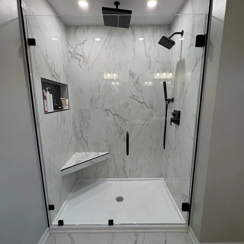 A frameless shower with matte black hinges and a black rain head, white marble-look tile