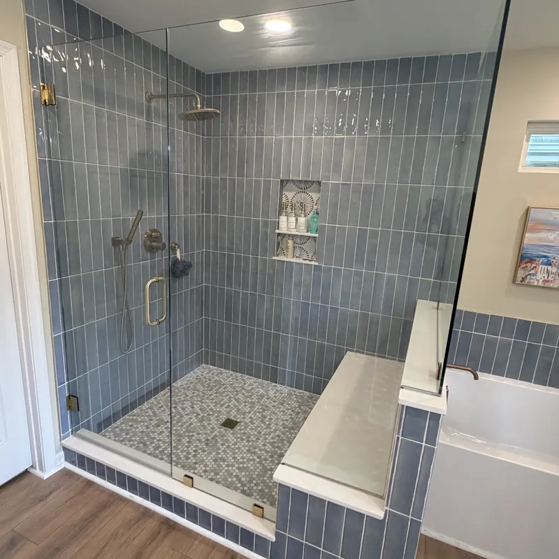 A frameless shower with satin brass hinges and pull, blue vertical tile and a bench