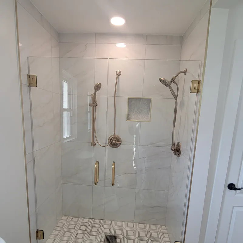 A frameless shower door with satin brass hinges and handles, white marble-look tile
