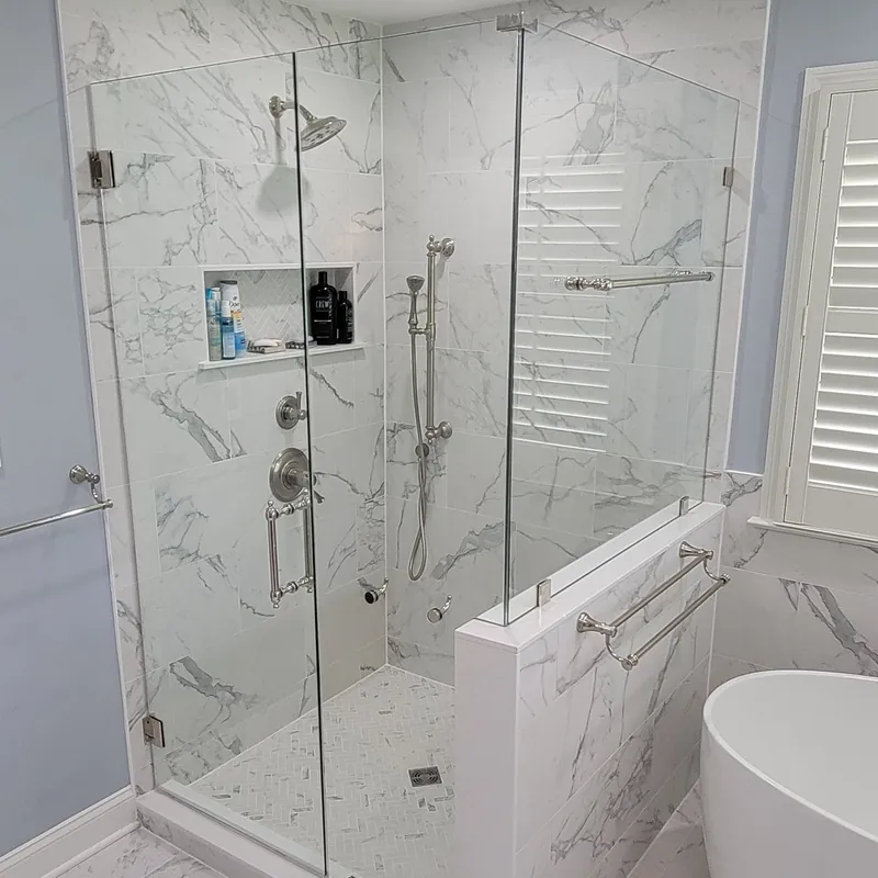 A frameless shower on a half wall with brushed nickel hinges and towel bar