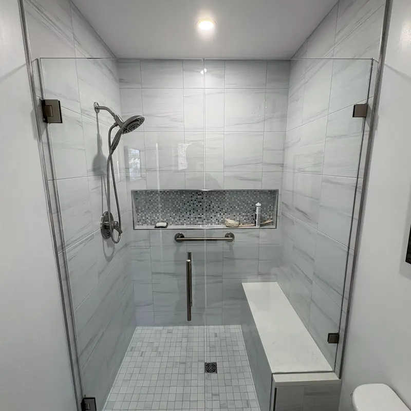 A frameless shower with brushed nickel hinges, a long tiled niche and a grab bar