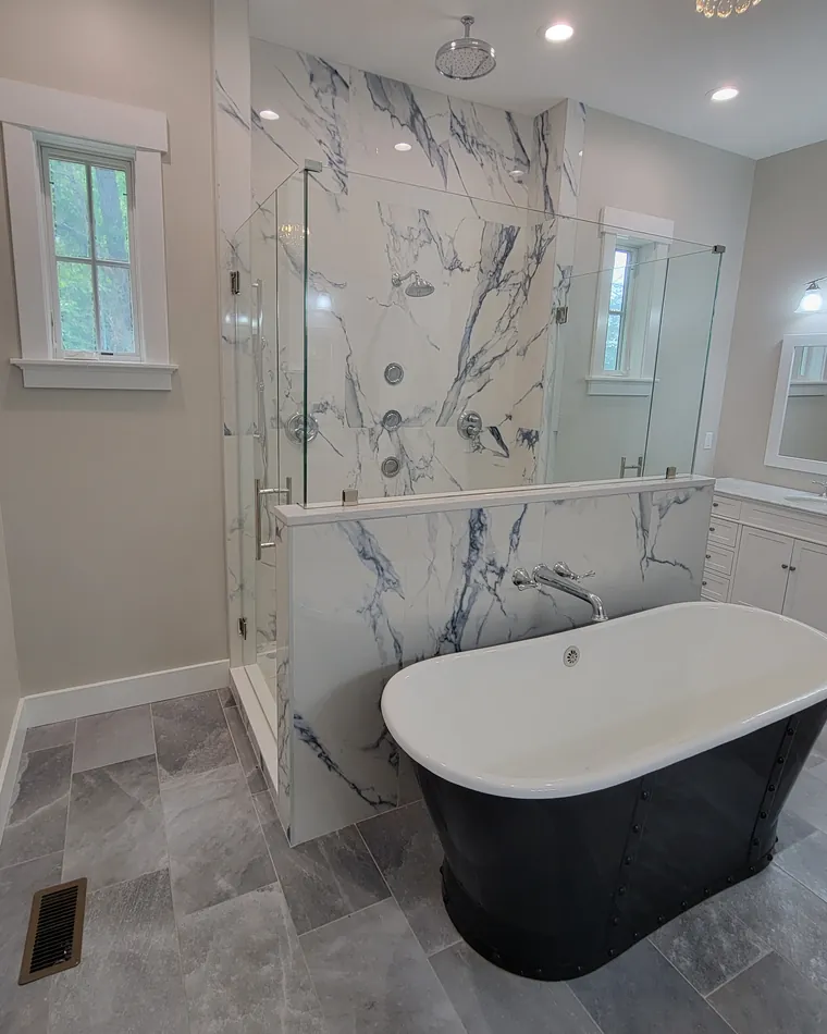 A glass panel on a marble half wall beside a black freestanding tub