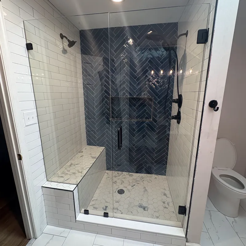 A frameless shower with matte black hinges, a navy herringbone tile wall and a bench