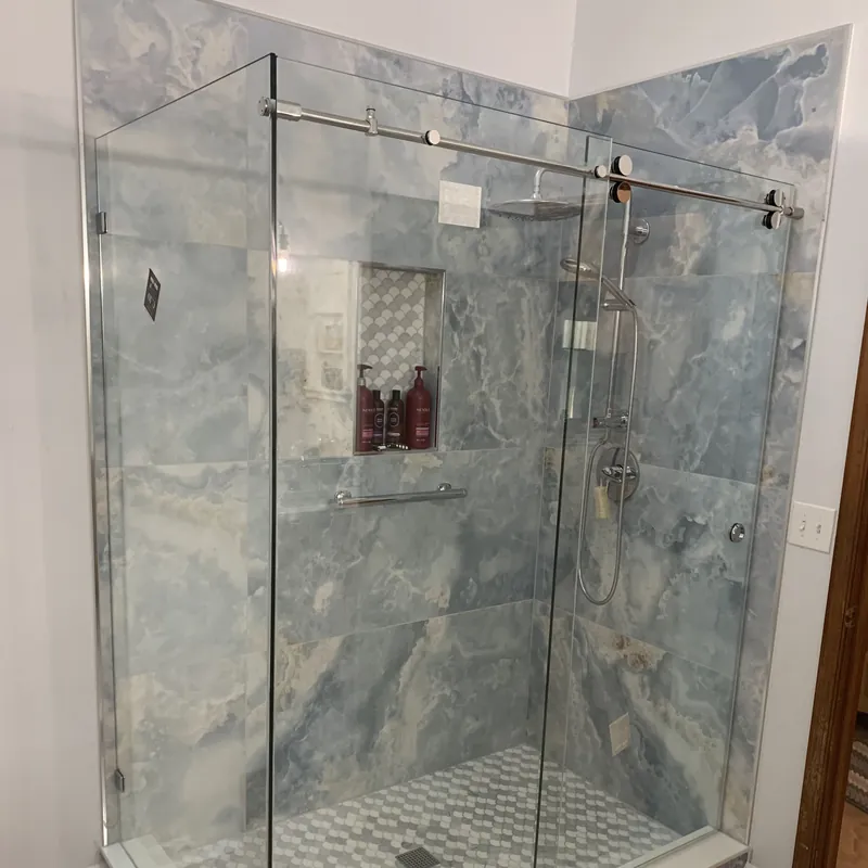 A sliding glass shower door on a polished rail, in front of blue marble-look tile